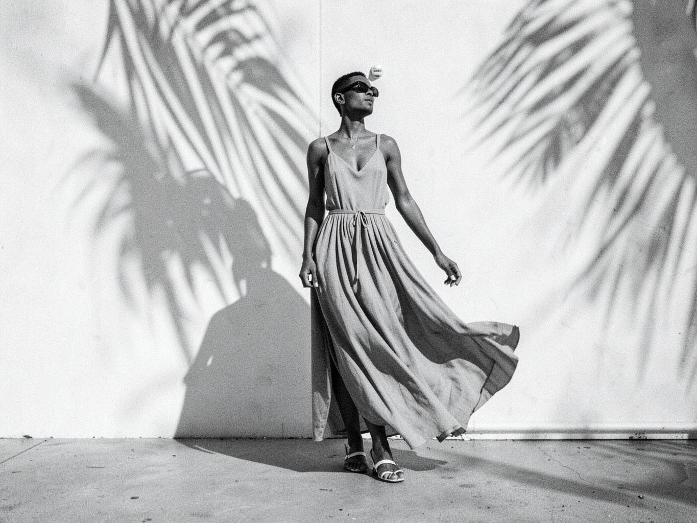 Modelo con vestido largo ante un muro blanco con sombras de palmeras